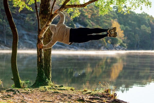 Ein Mann führt die Kraftübung „Menschliche Fackel“ an einem Baum am See aus. 