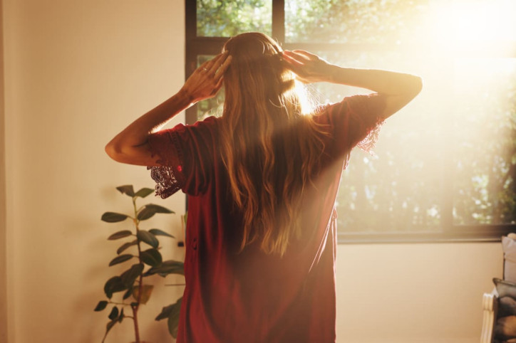 Eine Frau wird nach dem Aufstehen von der Sonne durchs Fenster geblendet