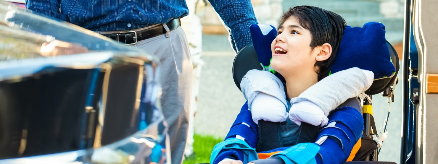 Ein Kind sitzt im Rollstuhl und wird von einem Erwachsenem geschoben.