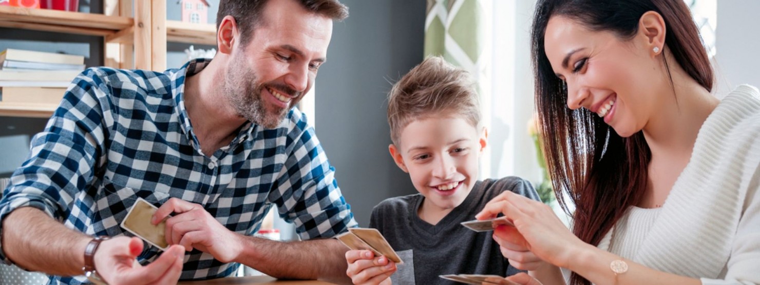 Eine junge Familie sitzt an einem Tisch und spielt gemeinsam ein Brett- und Kartenspiel.