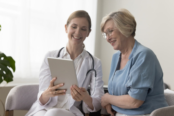 Junge Fachärztin zeigt älterer Patientin Befunde auf dem tablet