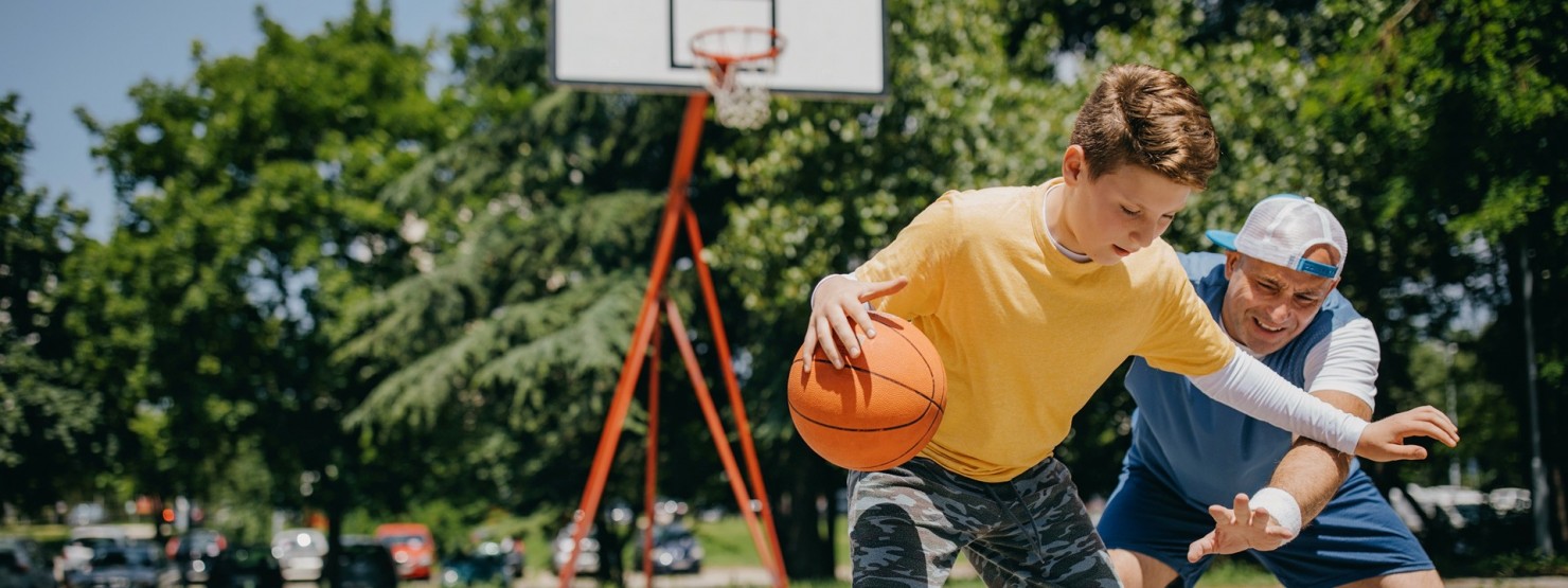 Ein Vater spielt mit seinem etwa 14-jährigen Sohn Basketball.