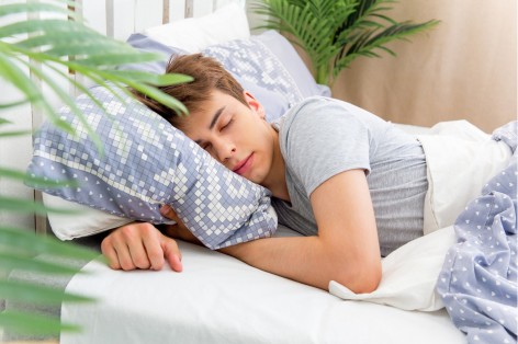 Junger Mann Anfang 20 liegt gemütlich im Bett und schläft.
