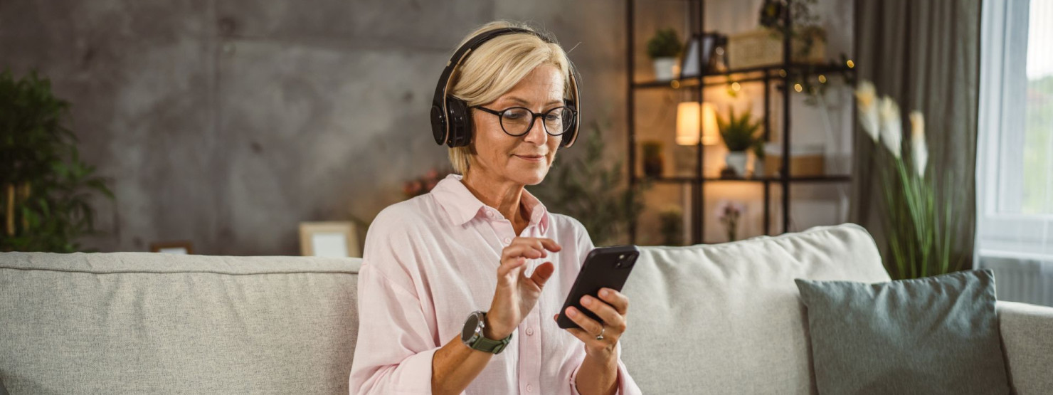 Eine Frau sitzt im Schneidersitz auf einer Coach und hört über Kopfhörer den AOK-Podcast zum Thema Pflege.