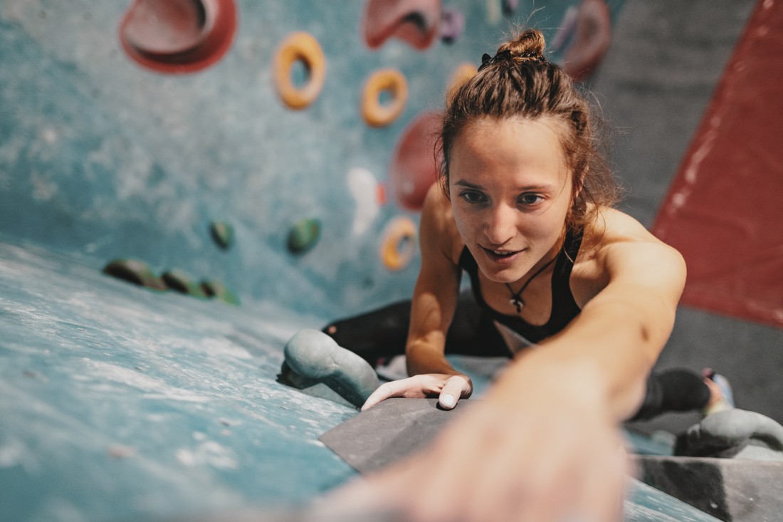 Eine etwa 20-jährige Frau klettert in einer Kletterhalle. Das Bild zeigt eine Vogelperspektive.