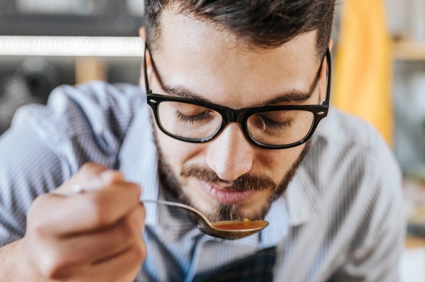 Junger Mann mit Brille kostet seine selbstgekochte Suppe.