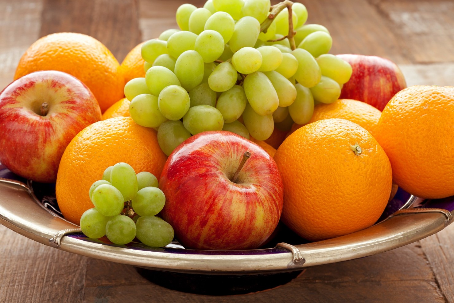 Eine Obstschale mit Weintrauben, Äpfeln und Orangen steht auf einem Tisch.