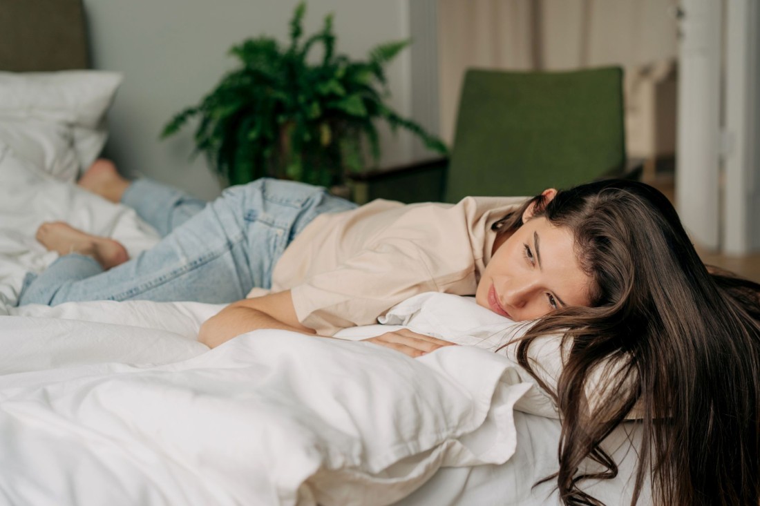 Junge Frau liegt mit fehlender Motivation auf ihrem Bett.