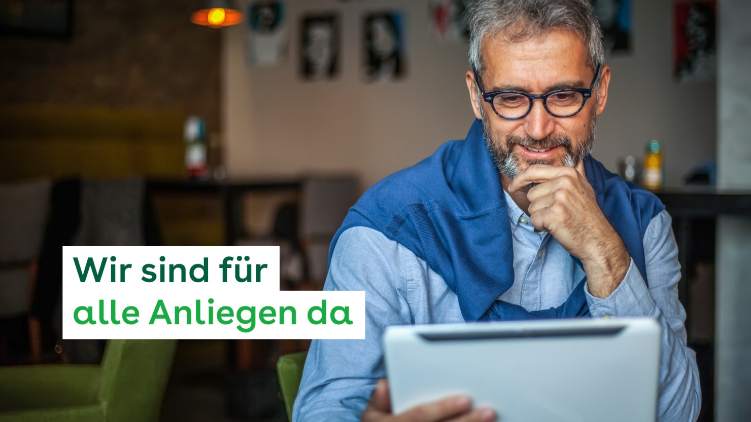 Ein etwa 55-jähriger Mann nutzt auf einem Tablet die Online-Services der AOK Sachsen-Anhalt. Er sitzt in einem Café, hält die linke Hand ans Kinn und lächelt.
