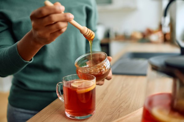 Nahaufnahme einer Frau, die Honig in eine Tasse Tee gibt.