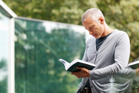 Ein Mann steht an einem Geländer und liest ein Buch.