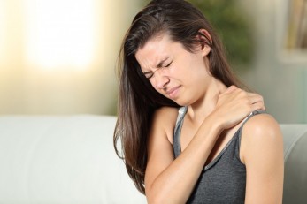 Ein etwa 14 jähriges Mädchen reift sich mit schmerzverzerrten Gesicht an ihre linke Schulter.