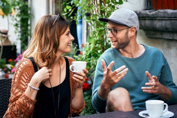 Ein 30-jähriger Student und eine 20-jährige Studentin sitzen vor einem Café und unterhalten sich.
