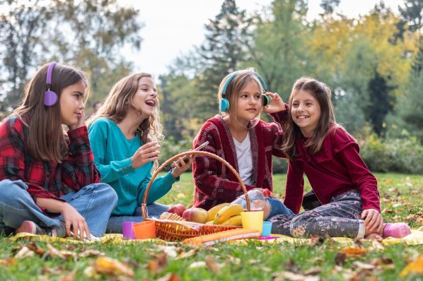 4 ca. 10-jährige Mädchen sitzen im park auf einer Decke und hören Musik über Kopfhörer