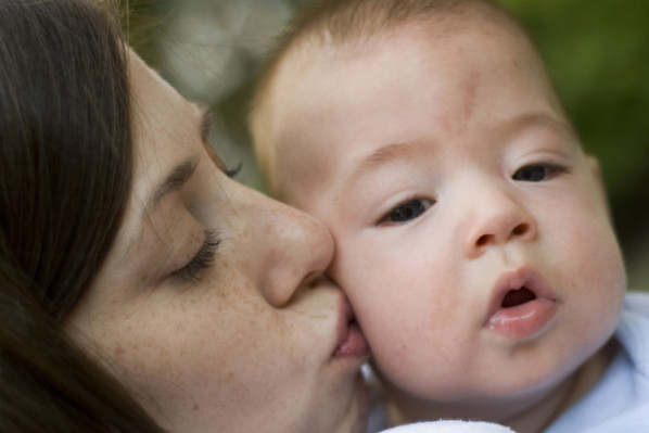 Eine Mütter küsst ihr Baby, mit Storchenbiss auf der Stirn, auf die Wange.