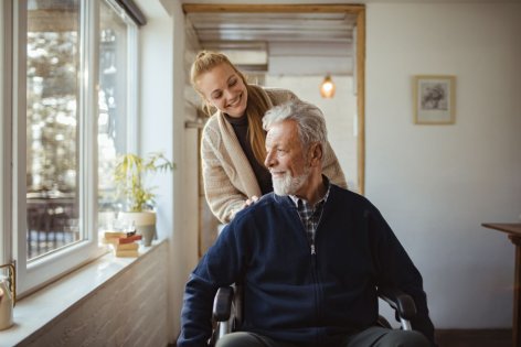 Eine Angehörige schiebt einen älteren pflegebedürftigen Mann im Rollstuhl.