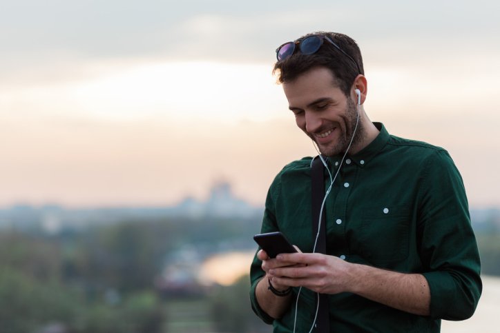 Ein etwas 35-jähriger Mann hört den Gesundheitswissen kompakt Podcast der AOK Sachsen-Anhalt auf seinem Handy.