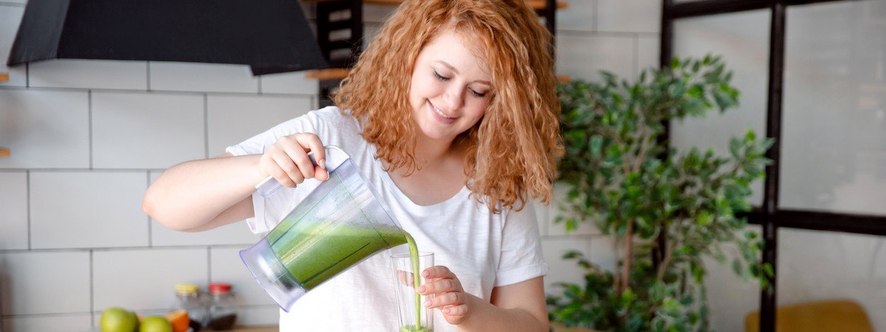 Rothaarige Frau gießt sich einen grünen Saft in ein Glas.