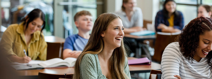 Studenten und Studentinnen sitzen nebeneinander auf einer Treppe und schauen auf einen Laptop.
