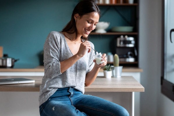 Eine etwa 30 jährige Frau löffelt Joghurt aus einem Glas.
