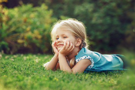 Kleines blondes Mädchen liegt auf grüner Wiese.