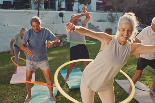 Ein Vater steht mit seiner etwa 8 jährigen Tochter im Garten. Beide spielen mit einem Hula Hoop-reifen und lachen dabei ausgiebig.