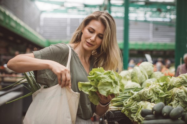 Junge Frau kauft auf dem gemüsemarkt einen salatkopf