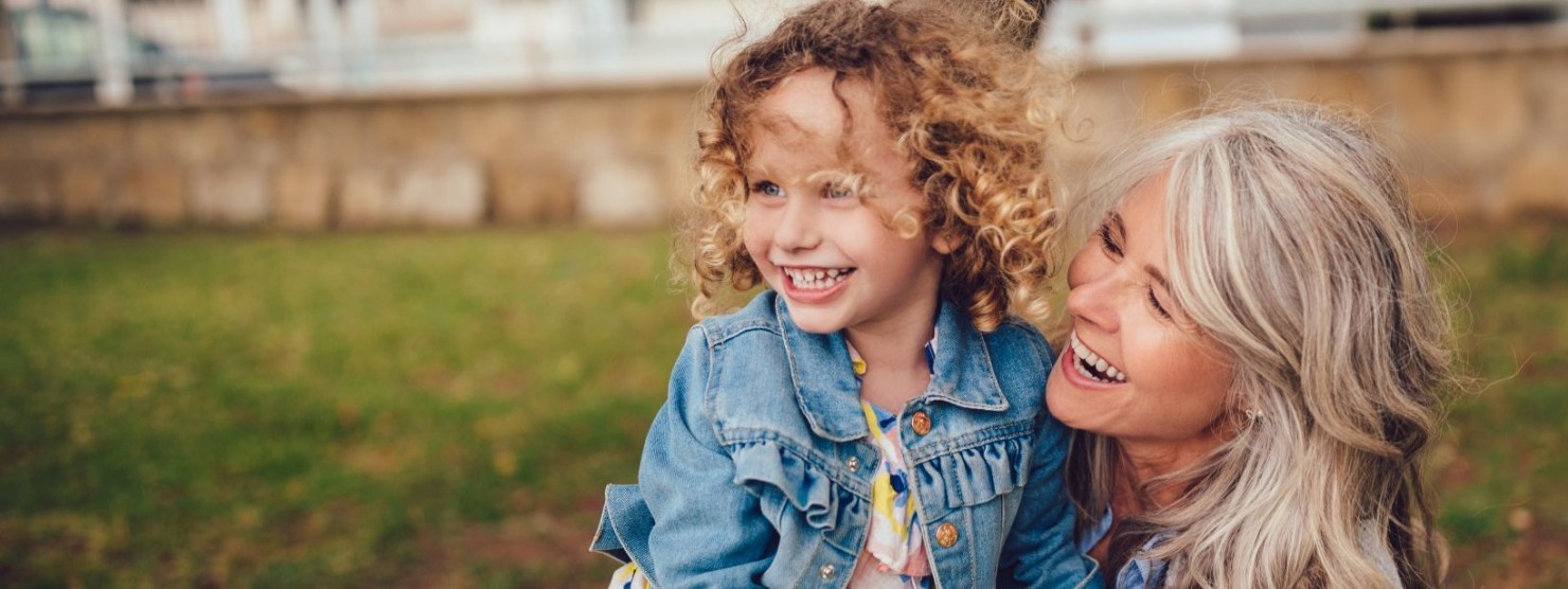 Eine Mutter spielt mit ihrer Tochter zusammen im Garten. Beide lachen ausgiebig.