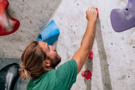 Ein junger Mann hängt an einer Kletterwand in einer Boulder-Halle.