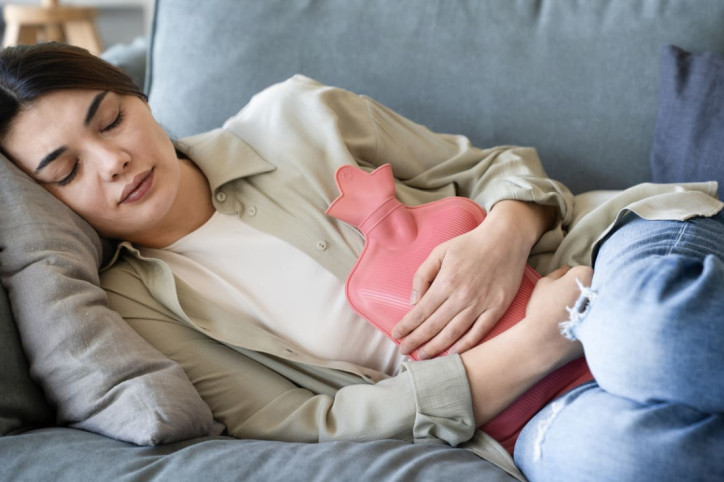 Eine Frau liegt mit Schmerzen aufgrund der Periodengrippe auf dem Sofa