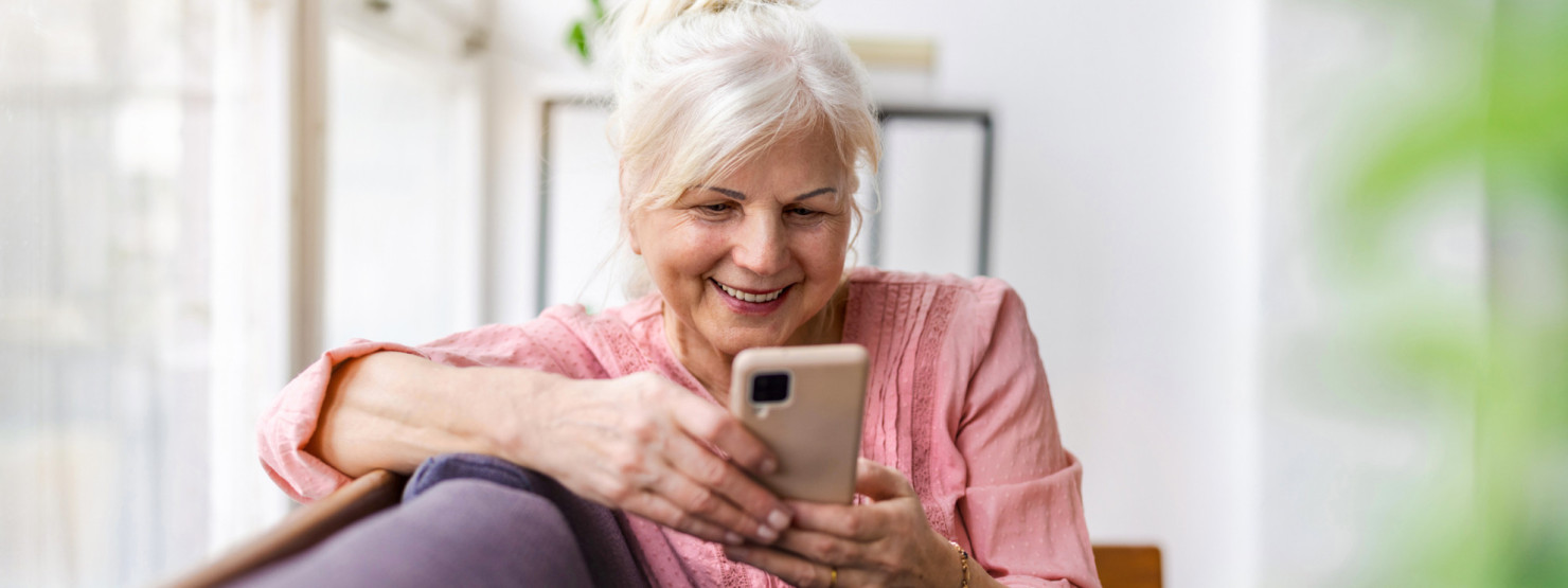 Eine Seniorin schaut freudig auf ihr Handy und ruft die Servicestelle 116 117 an.