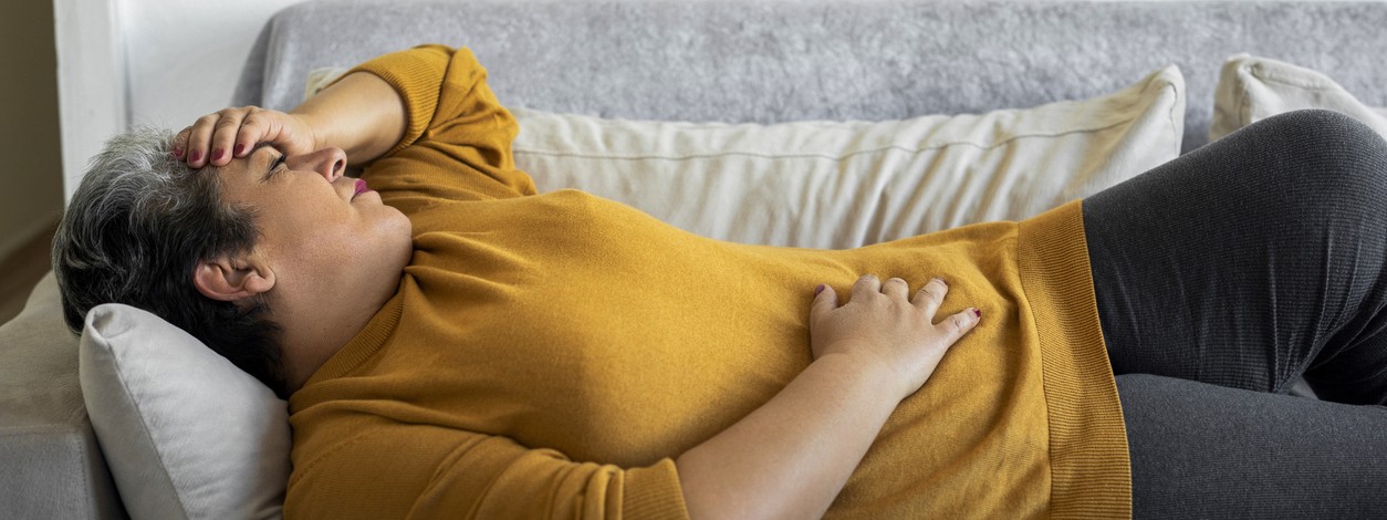 Eine Frau, die an Aneurysmen leidet, liegt mit Schmerzen auf dem Sofa.