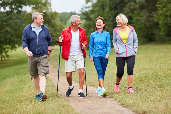Eine 4-köpfige Gruppe von etwa 55 Jährigen laufen einen Naturweg entlang. Alle vier lachen ausgiebig und unterhalten sich.