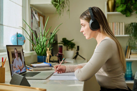 Eine junge Frau nimmt zuhause an einem medizinischem Online-Seminar teil und macht sich dabei Notizen.