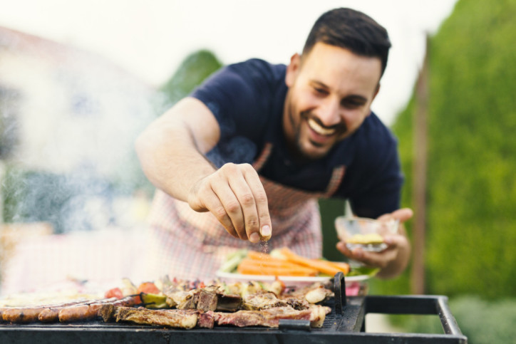 Ein Mann würzt sein Essen auf dem Grill.