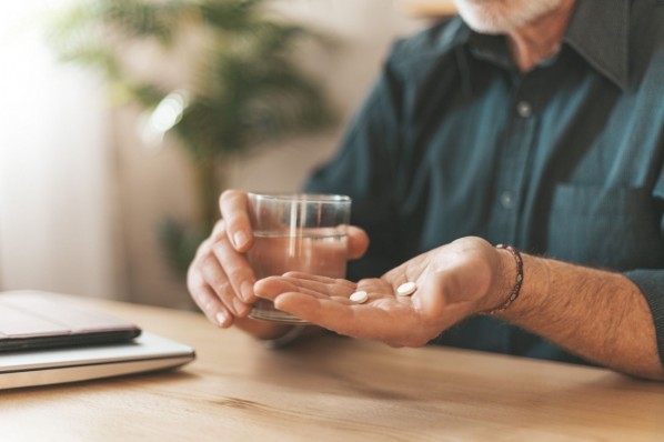 Ein Mann hält in der linken Hand Tabletten und in der rechten Hand ein Glas Wasser.