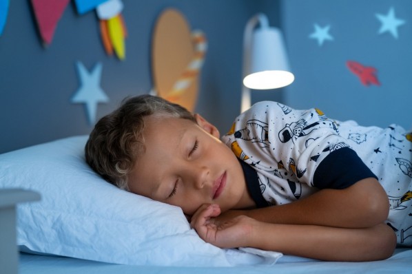 Kleiner Junge schläft im bett. Seine Zimmerwand ist mit Planeten dekoriert. Es brennt das Licht der nachttischlampe
