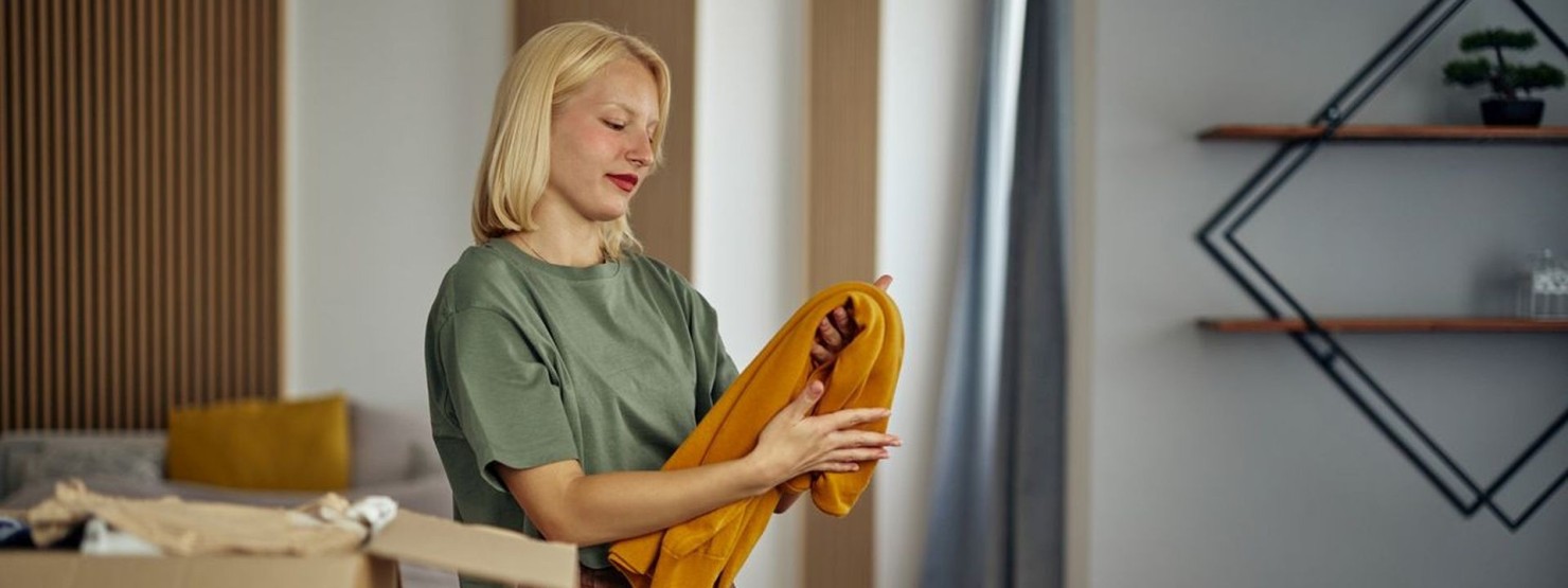 Eine etwa 30 jährige Frau sortiert Kleidung nach dem Minimalismus-Prinzip durch.