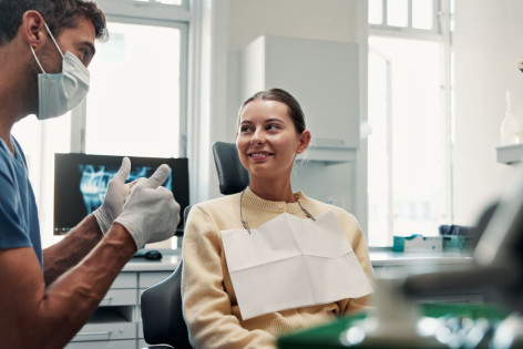 Ein freundlicher Zahnarzt erklärt einer Patientin auf dem Behandlungsstuhl sein Vorgehen.