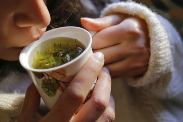 Eine etwa 30-jährige Frau trinkt einen warmen Tee mit verschiedenen Heilkräutern.