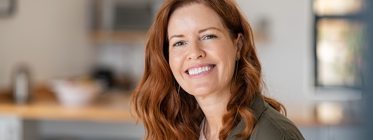 Frau Anfang 40 mit langen roten Haaren zeigt strahlendes Lächeln
