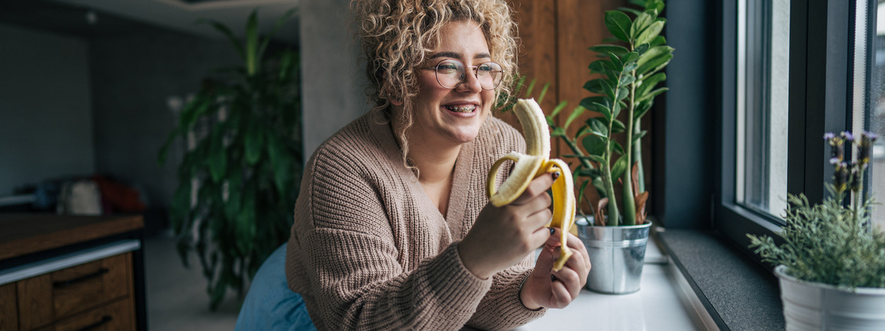 Frau lehnt an der Küchentheke und isst eine Banane