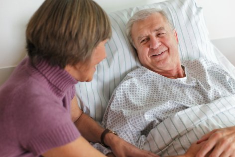Ein älterer Mann liegt im Bett un spricht mit einer Frau.