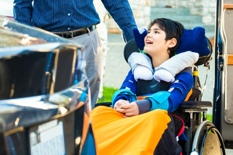 Ein Kind sitzt im Rollstuhl und wird von einem Erwachsenem geschoben.