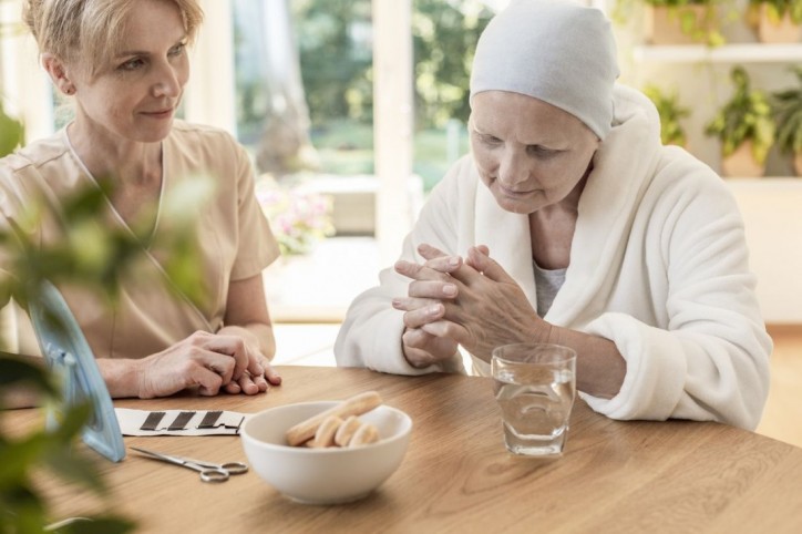 Eine schwerkranke Frau sitzt gemeinsam mit einer Pflegerin an einem Tisch.