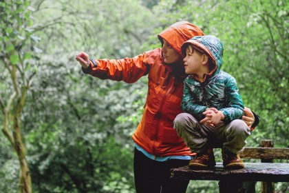Mutter zeigt Sohn etwas mit Regenkleidung im Wald.