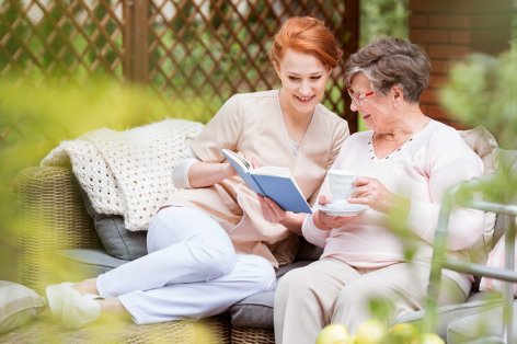 Pflegerin liest einer Seniorin vor