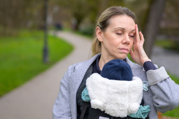 Eine Frau fühlt sich von Care-Arbeit für ihr Kind erschöpft