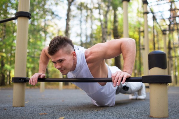 Ein junger Mann macht Liegestüzte an einer niedrig angebrachten Stange im Calisthenics-Park.