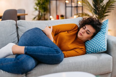 Eine Frau mit Schmerzen durch Adenomyose liegt auf dem Sofa